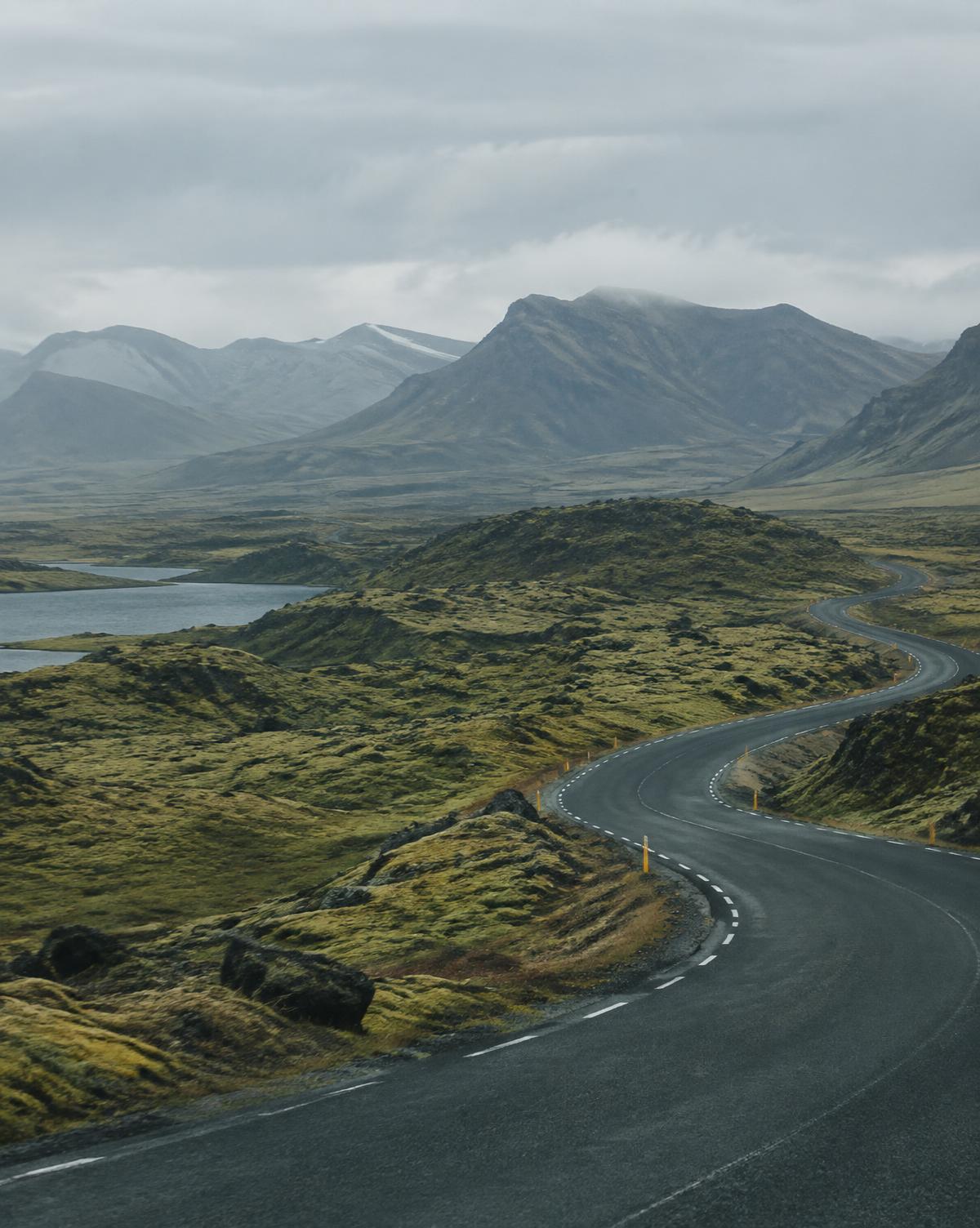 Empty road curving through mossy volcanic landscape beneath low Icelandic mountains