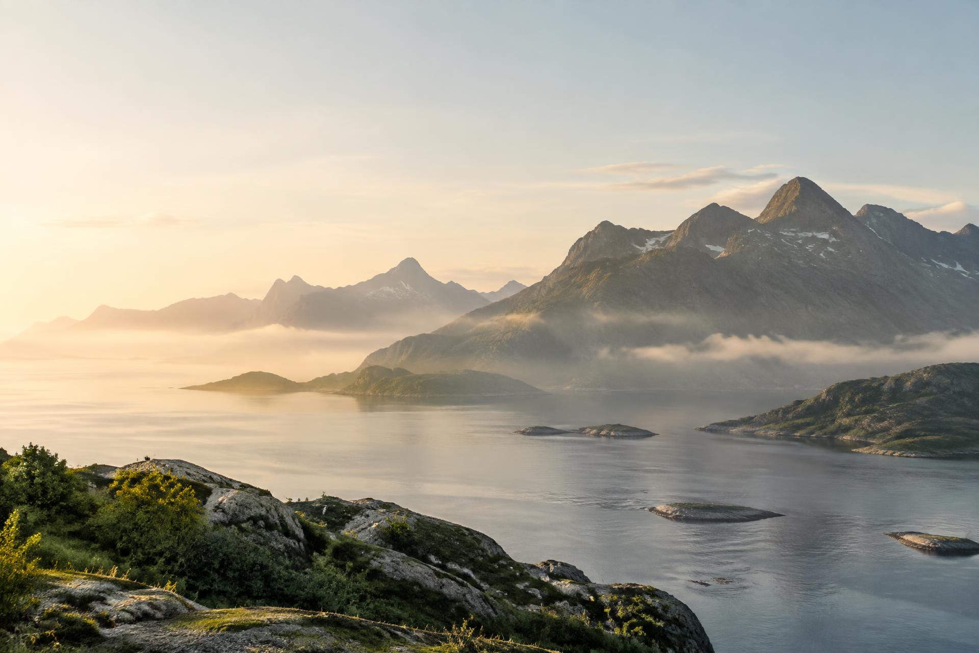 Mist drifting over a calm fjord beneath mountains at sunrise